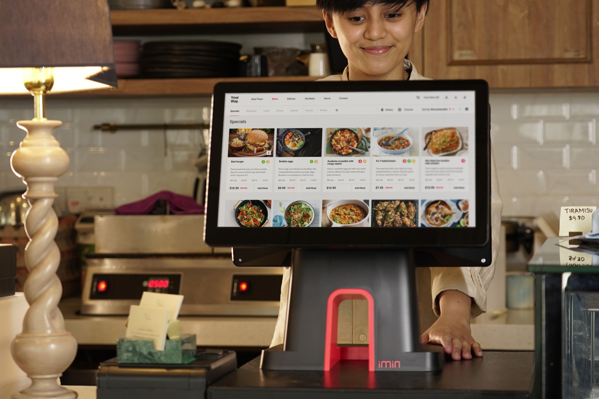 Restaurant staff member using a touchscreen POS system displaying a digital menu for AI ordering and online order management.